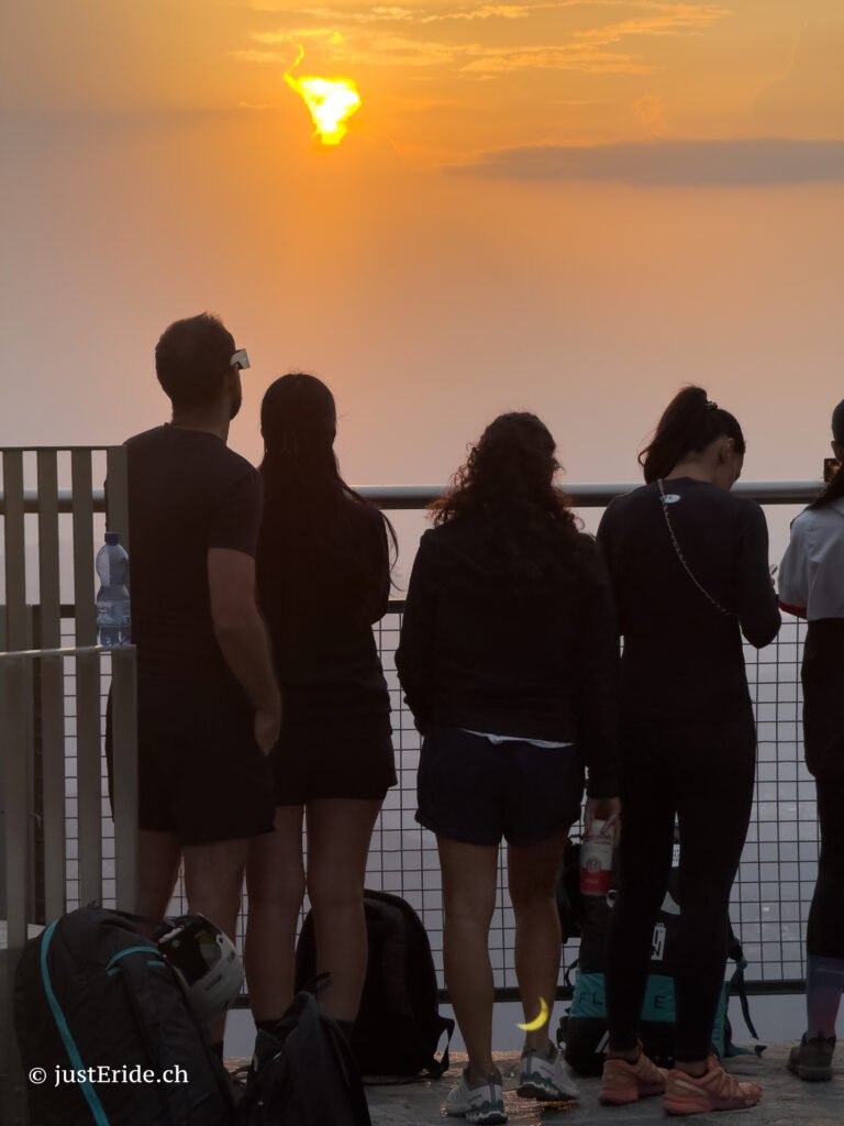 Silhouettes of people watching the partial solar eclipse at sunset from the panoramic terrace of Monte Generoso.